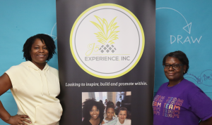 two women stand with a banner smiling at the camera