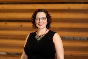 woman with glasses smiles in front of wooden wall
