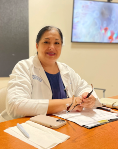 woman sits at desk with glasses in hand smiling