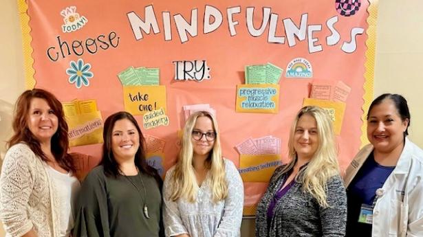 Five people stand behind mindfulness poster on wall.