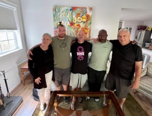 four men and one woman standing with their arms around each other smiling