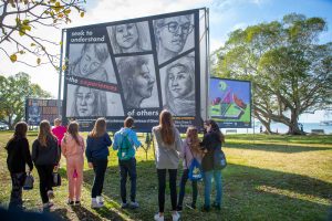 nine students gather around a billboard sized work of art