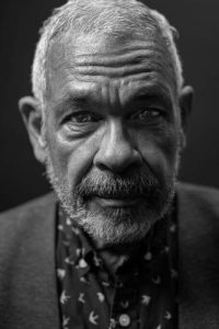 older man stares directly at the camera in black and white