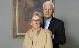 man and woman smiling in front of a painting hung on a wall